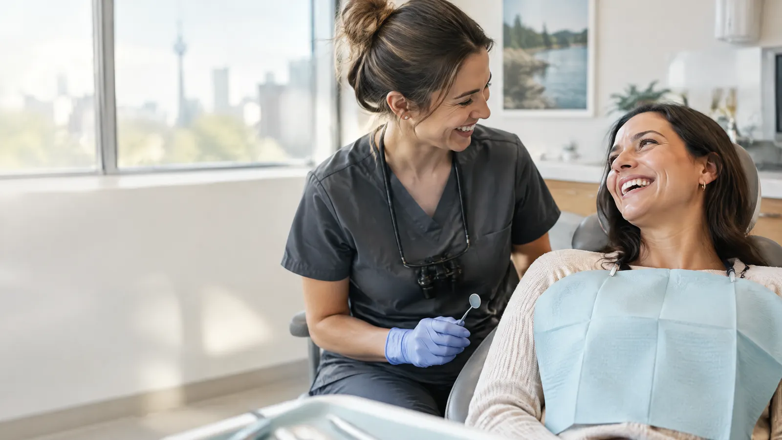 A woman in her thirties laughs with her dental hygienist after a cleaning in a bright, modern Ontario dental clinic.