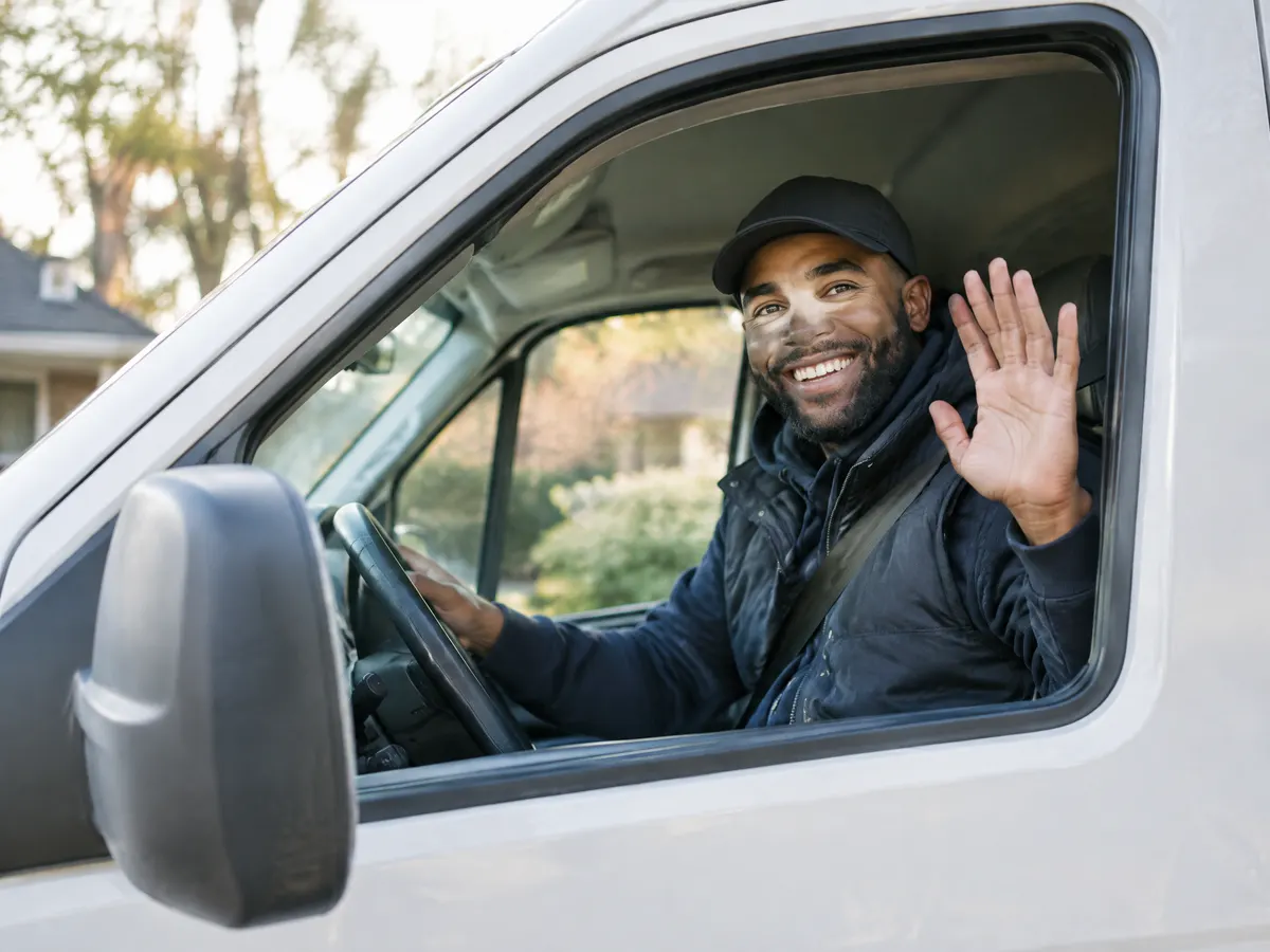 A delivery driver giving a wave from the cab of his van.
