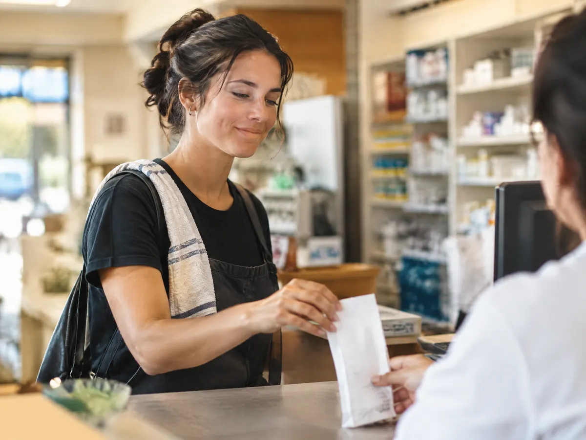 A server picking up a prescription at a pharmacy counter after a shift.