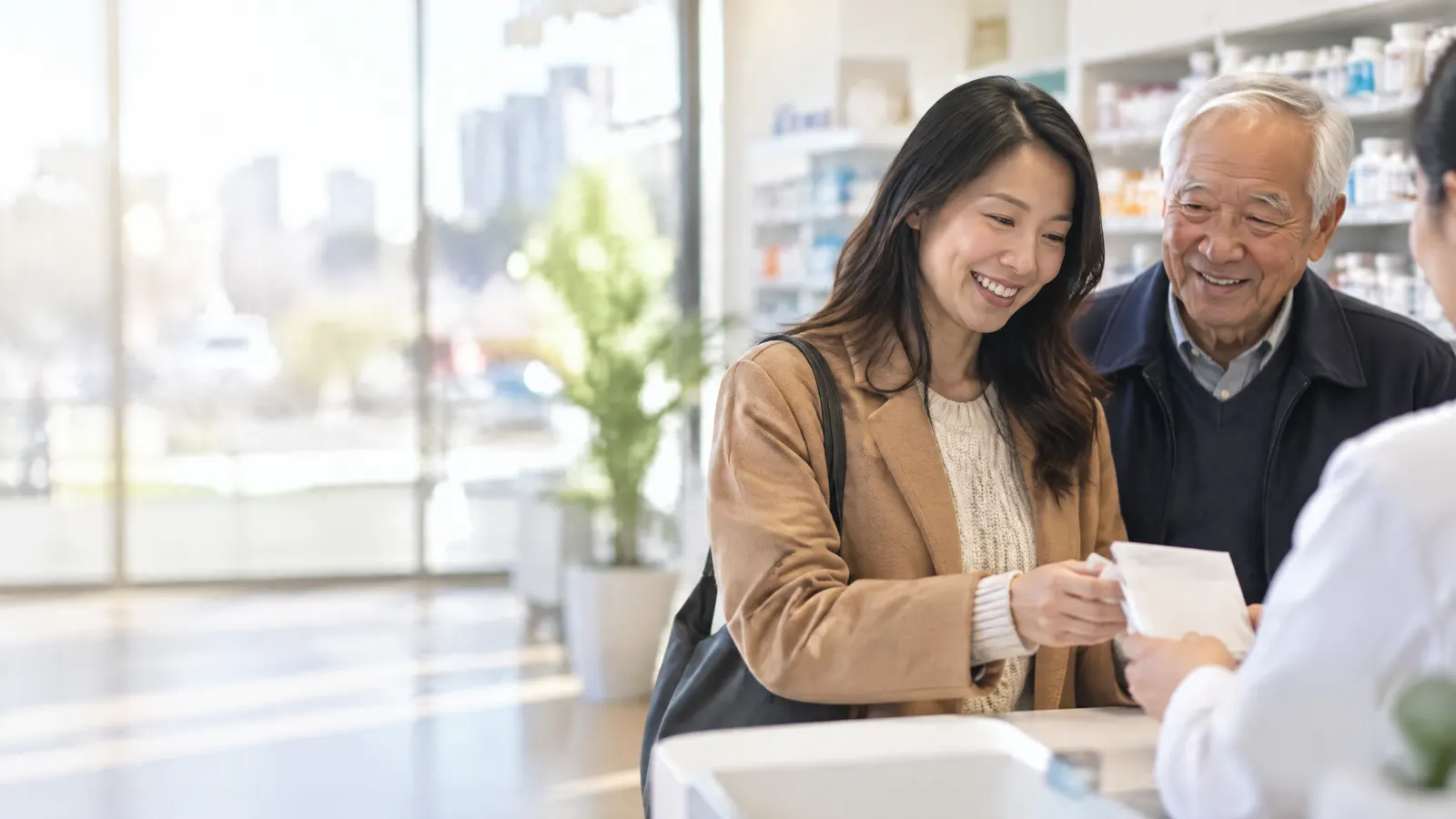 A woman in Markham picking up a prescription at a bright pharmacy with her elderly father, both smiling.