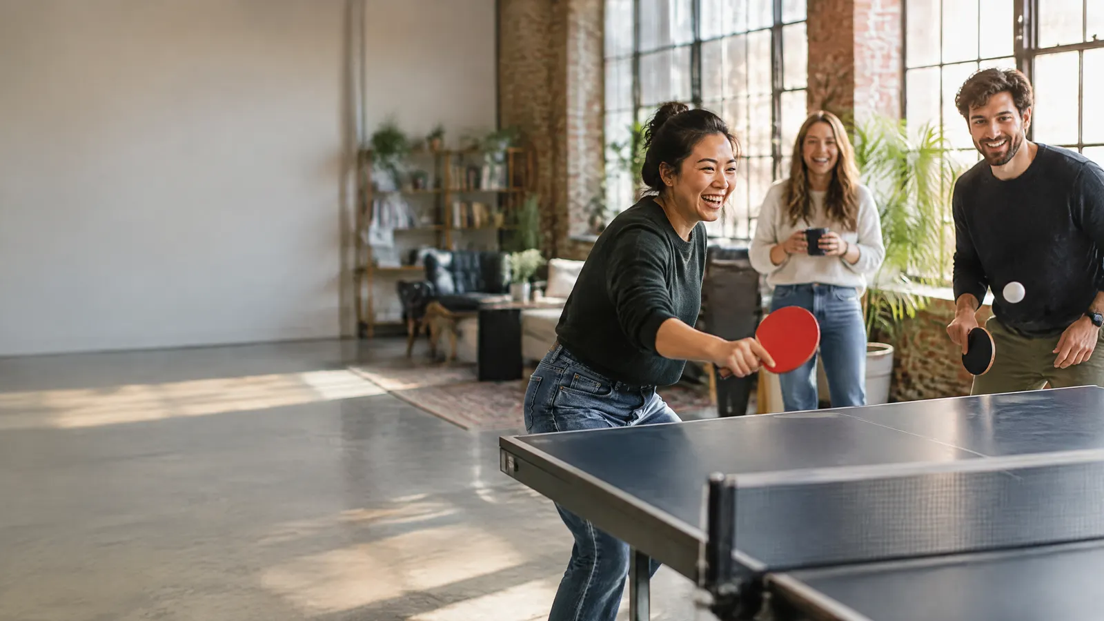 A young startup team playing table tennis in a loft workspace, relaxed and laughing.